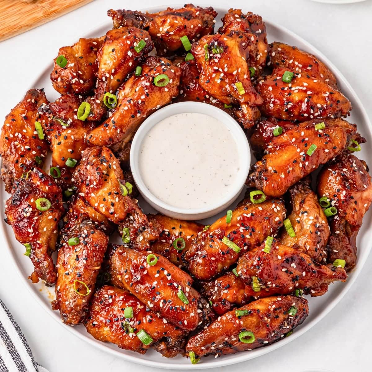 A plate of glazed chicken wings with ranch dip, garnished with green onions.
