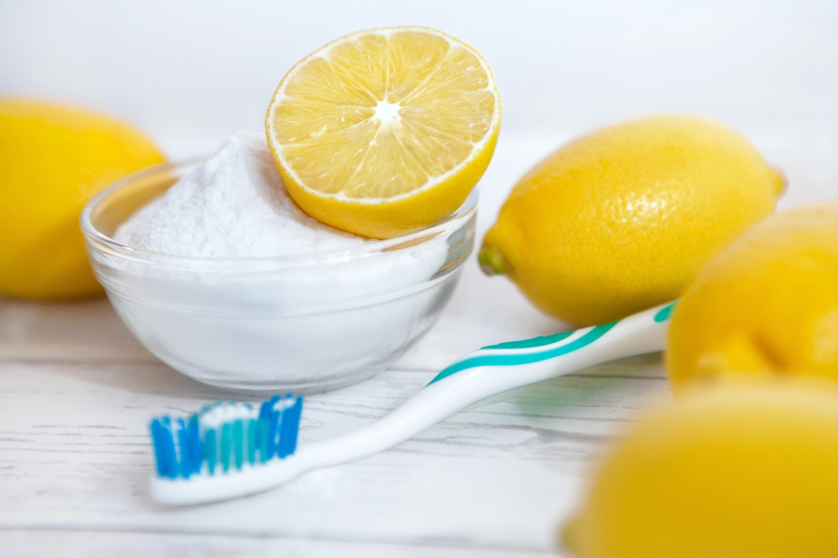 A bowl of baking soda, a halved lemon, whole lemons, and a toothbrush.