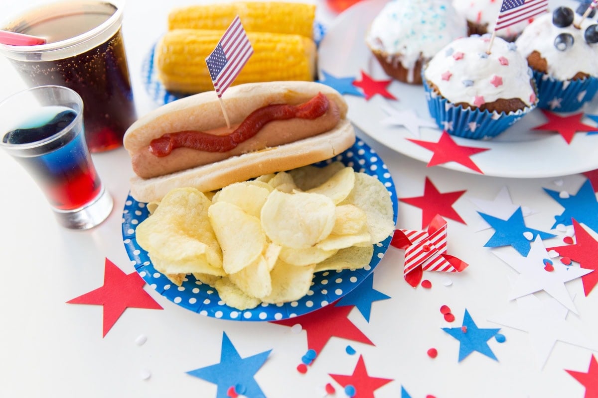 Hot dog, chips, and drinks on a festive 4th of July table with red, white, and blue.