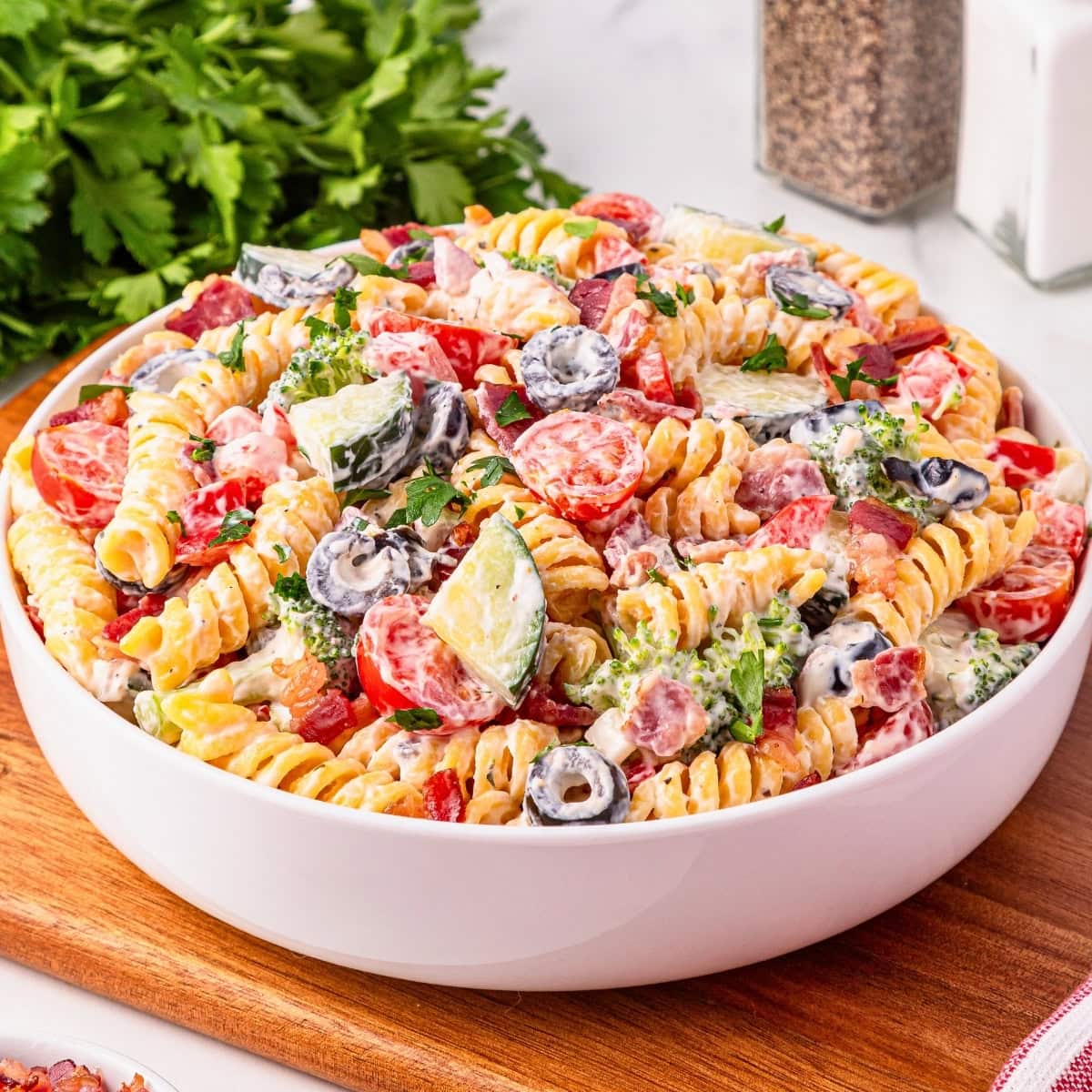 A bowl of creamy Bacon Ranch Pasta Salad with vegetables and olives on a board.