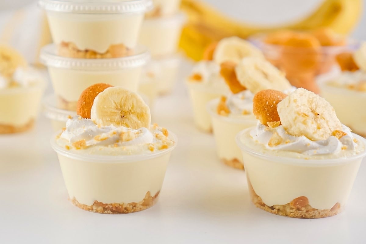 Mini banana pudding cups topped with banana slices and cookies on a white surface.
