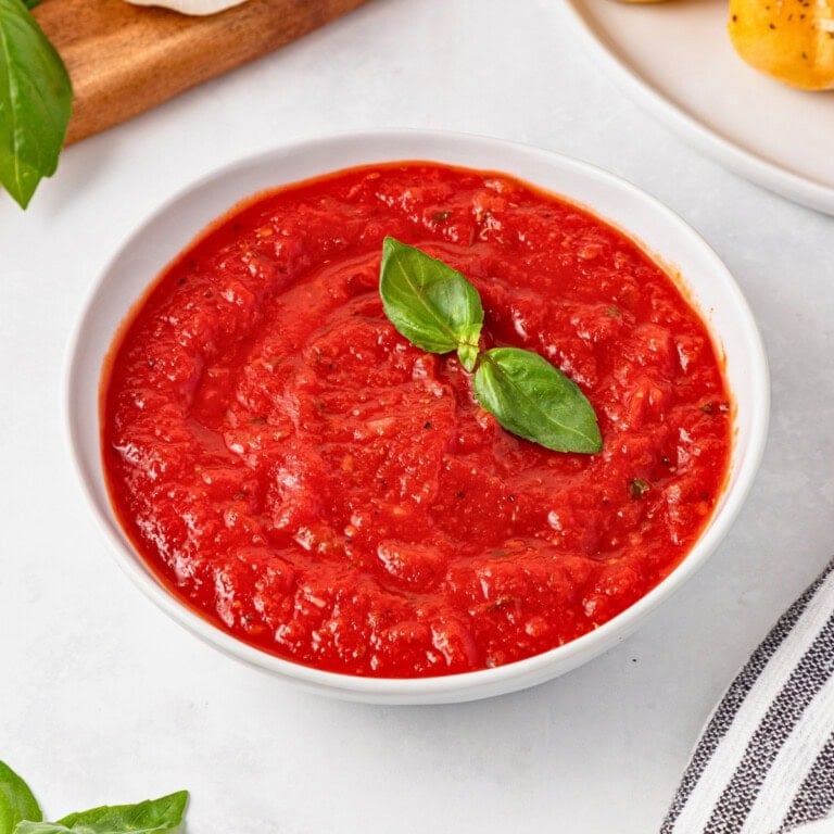 Bowl of best homemade marinara sauce garnished with fresh basil leaves.