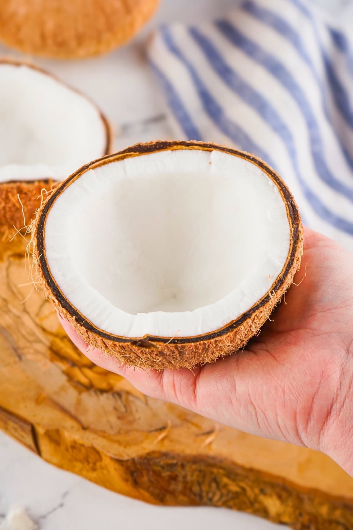 A hand holding half of a hollowed-out coconut with white flesh.