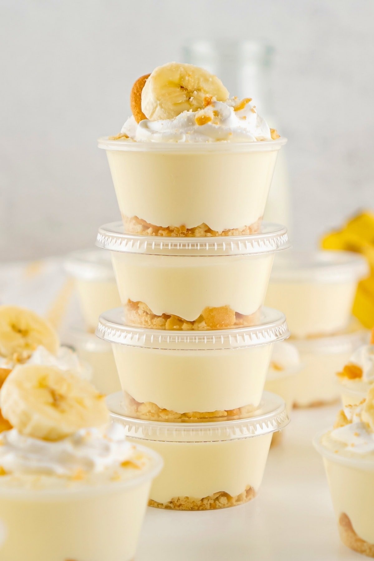 Stacked banana pudding cups topped with whipped cream, banana slices, and crumbs.