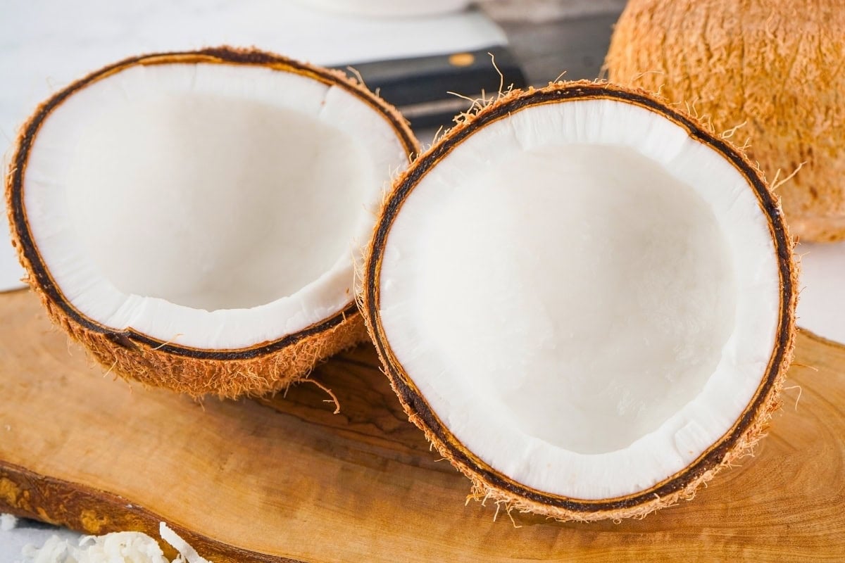 Two halves of a fresh coconut displayed on a wooden surface.