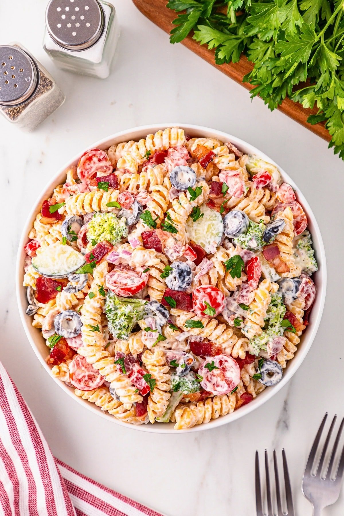 A bowl of creamy pasta salad with veggies and herbs on a white table.