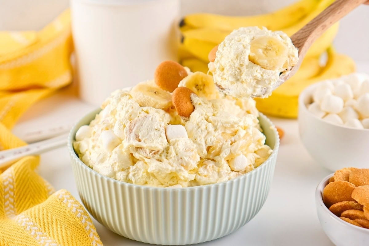 Bowl of banana pudding with vanilla wafers and marshmallows, spoonful above.