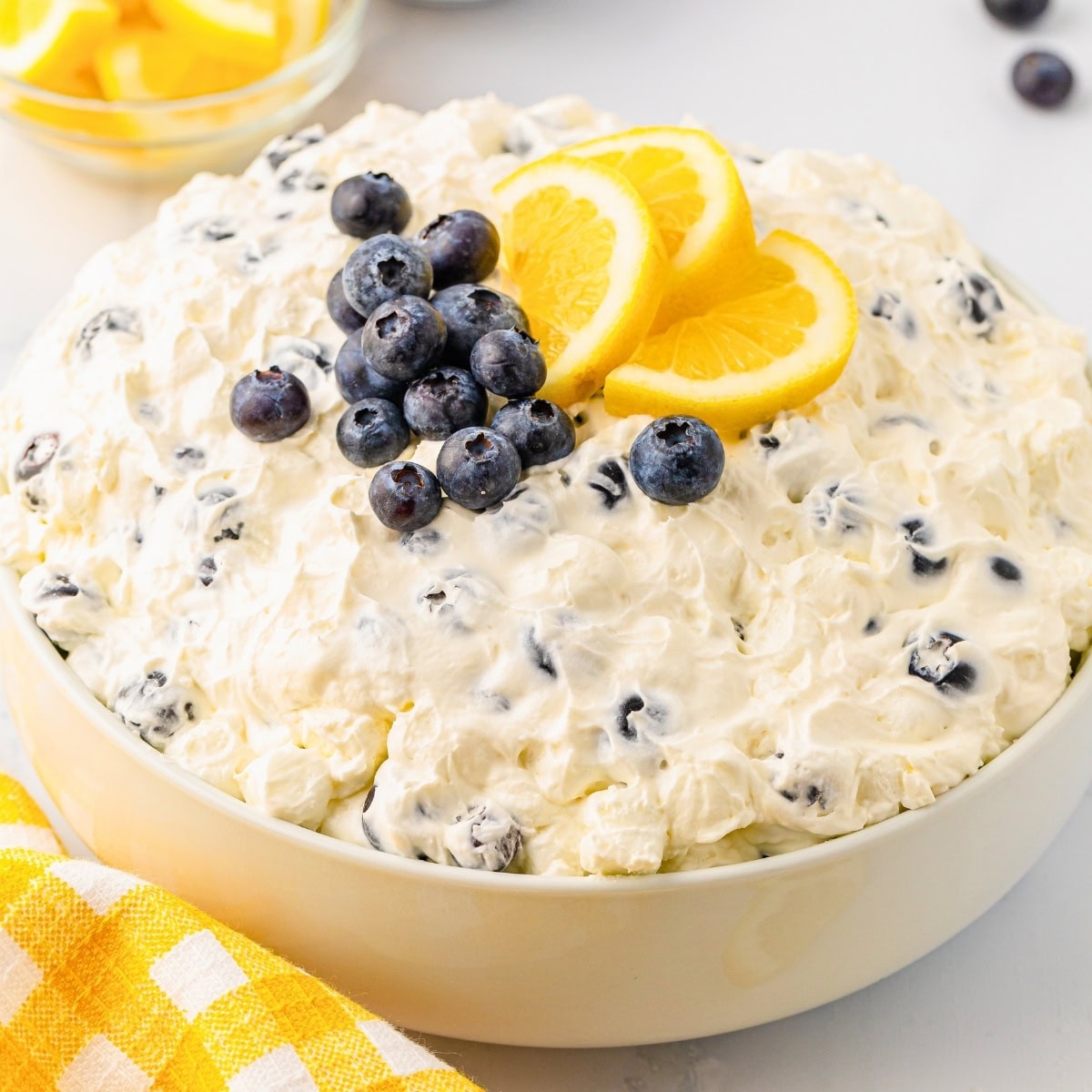 Creamy fruit salad topped with fresh blueberries and lemon slices in a white bowl.