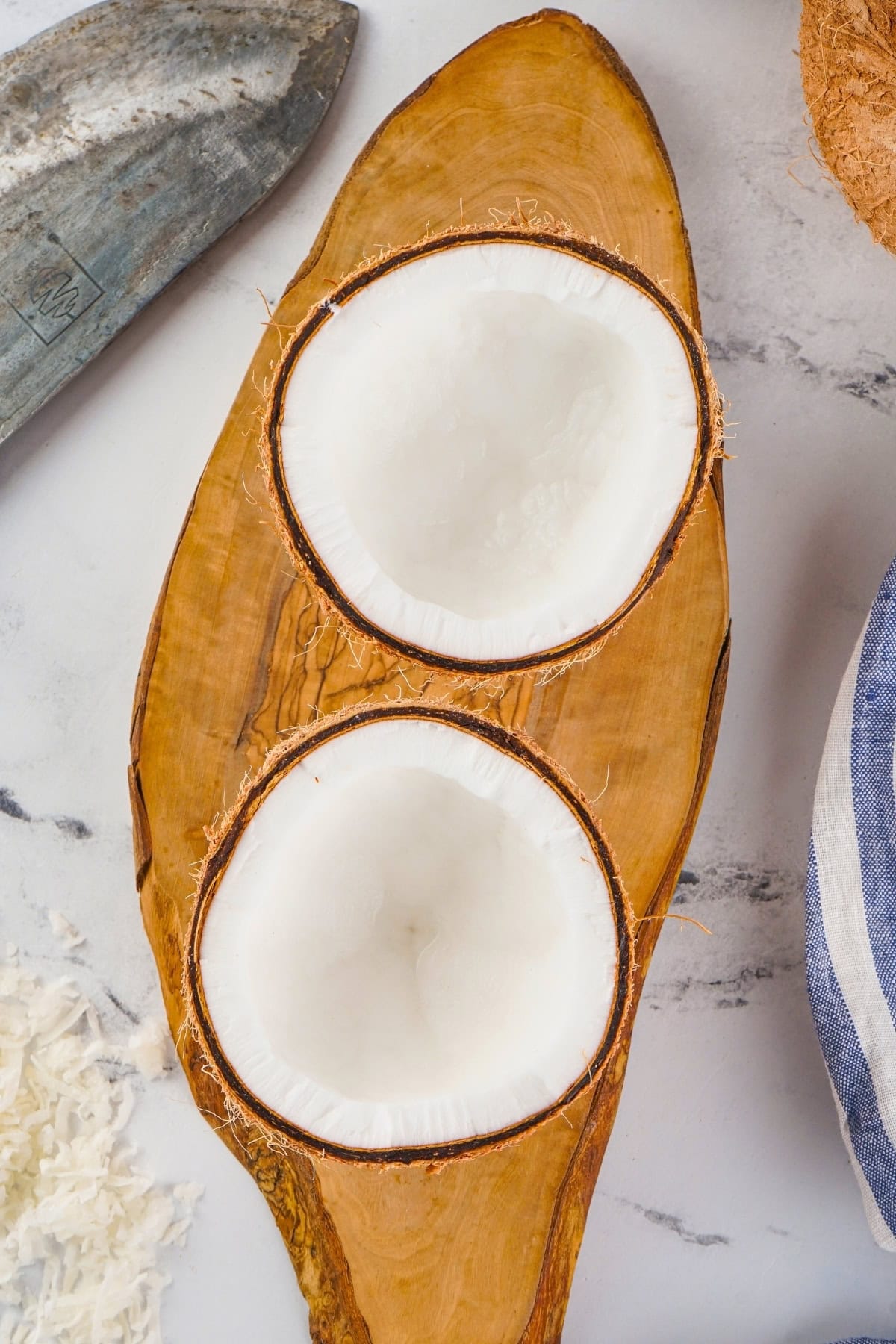 Two coconut halves placed on a wooden board with a knife nearby.