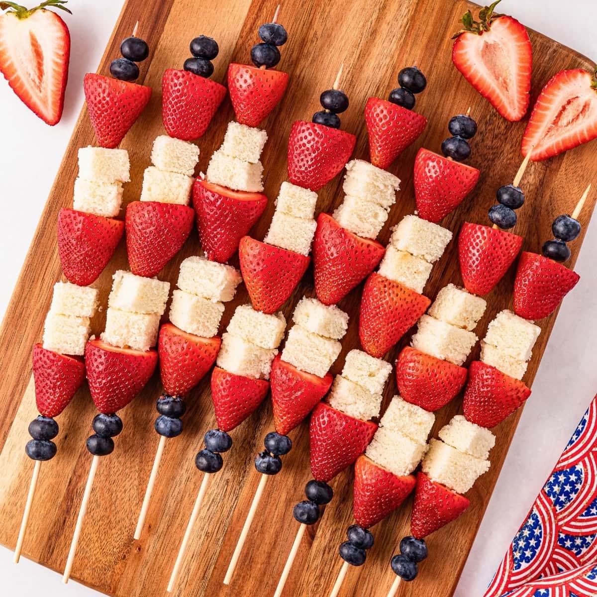 Fruit and cake skewers with strawberries, blueberries, and cake on a wooden board.