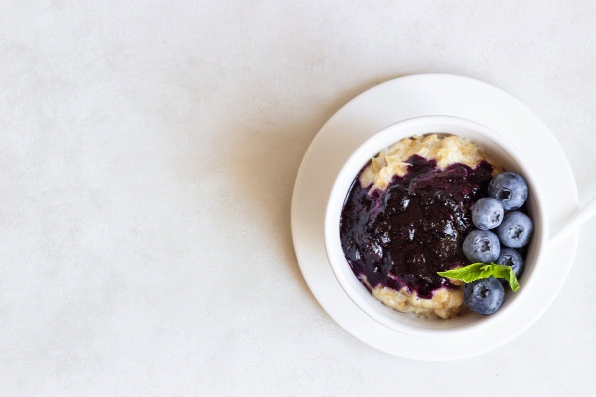 Bowl of oatmeal with blueberry sauce and fresh blueberries on a white table.