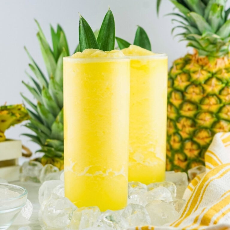 Two tall glasses of pineapple aqua fresca with ice and whole pineapples.