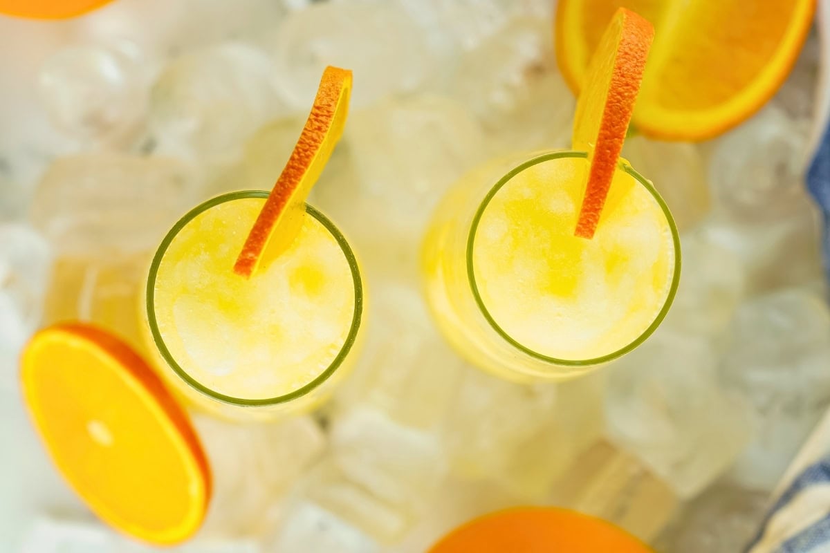 Two frozen mimosas with orange slices on ice cubes, viewed from above.