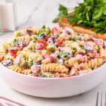 A bowl of creamy pasta salad with vegetables and herbs on a white table.