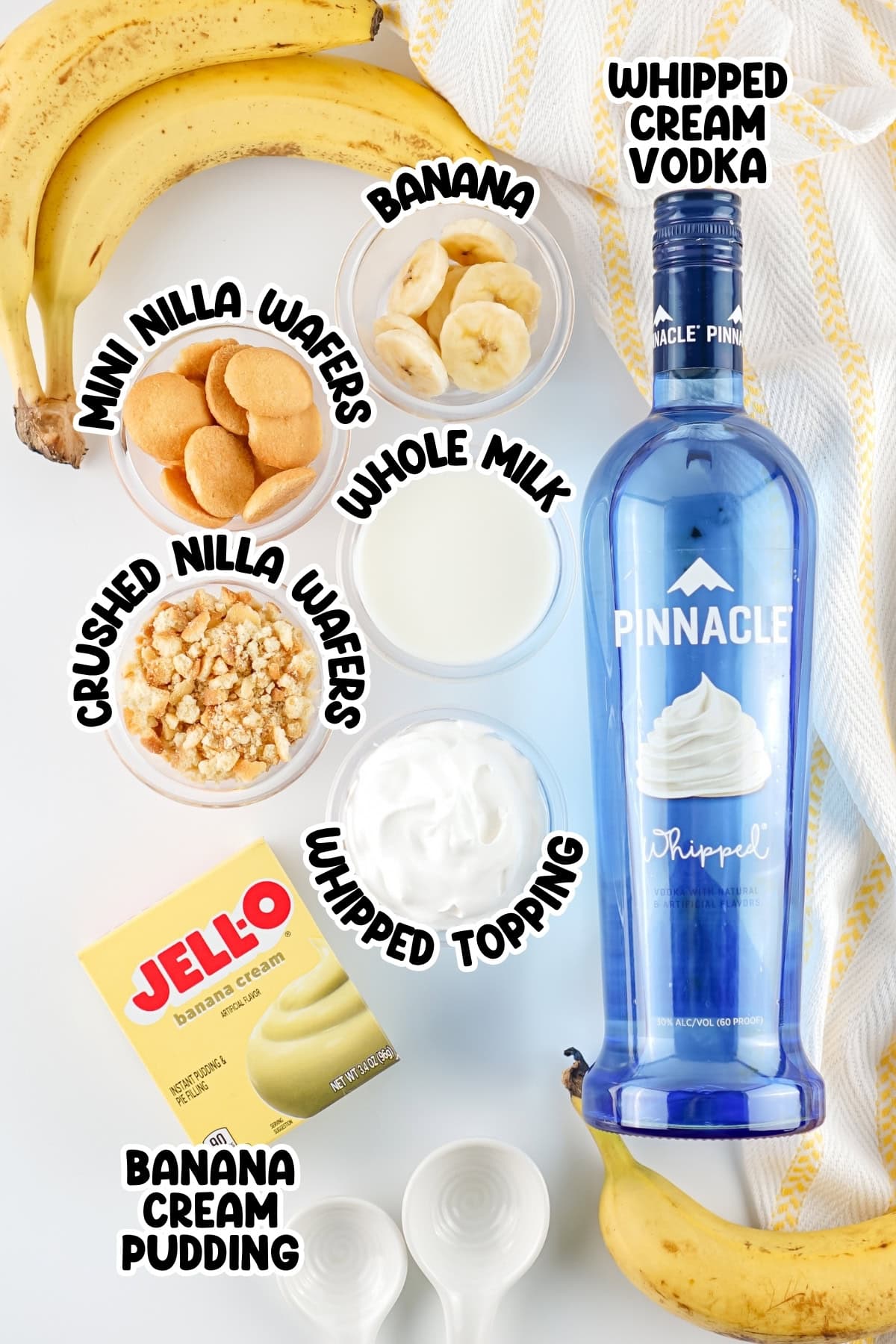 Banana pudding ingredients and whipped cream vodka arranged on a white surface.
