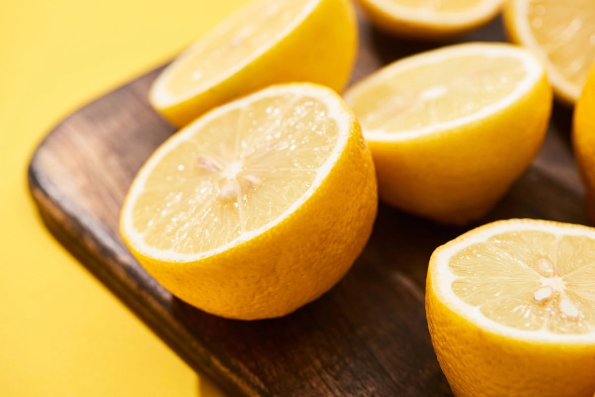Halved lemons on a wooden cutting board against a yellow background.