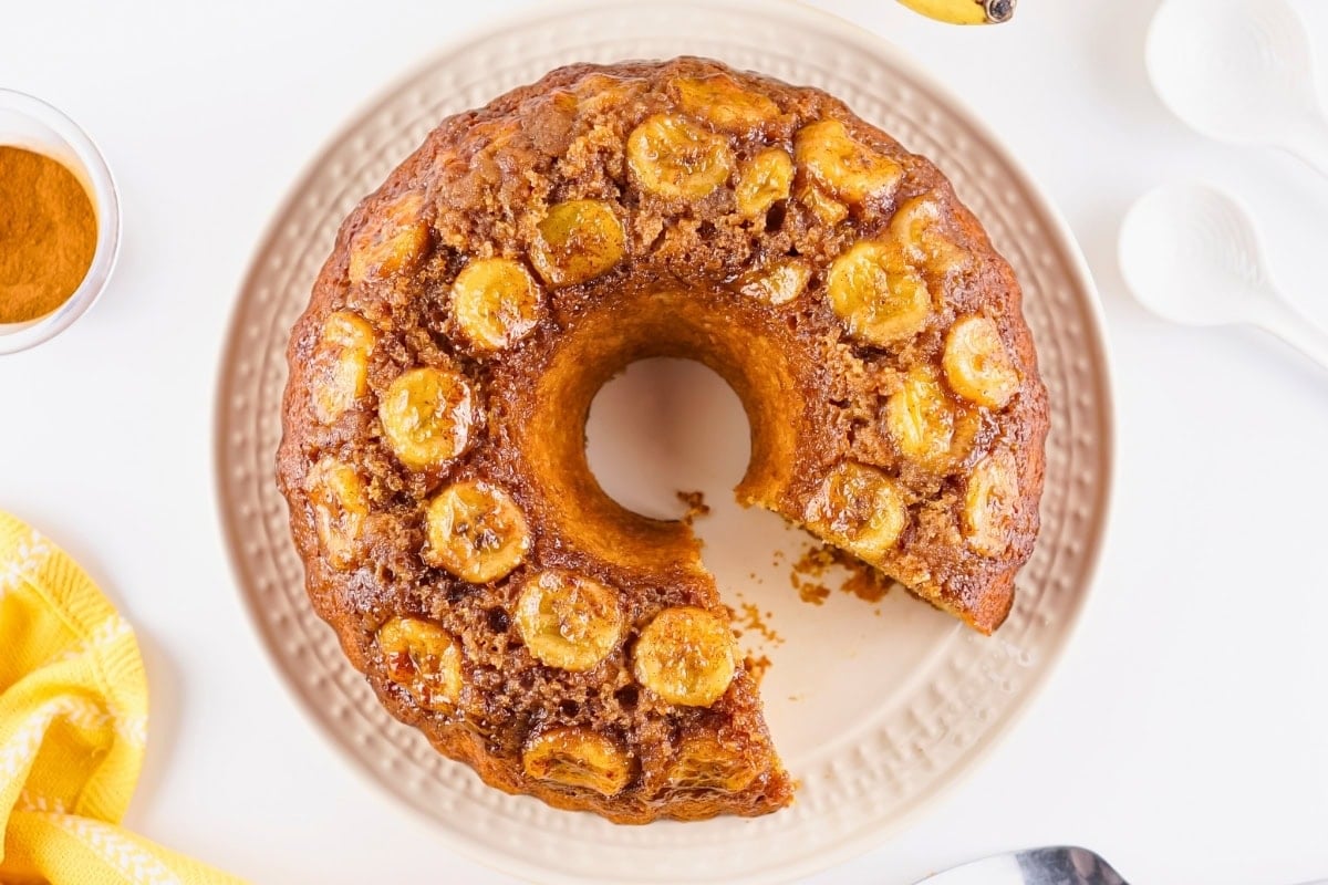 Bundt cake topped with banana slices on a plate, with one slice missing.