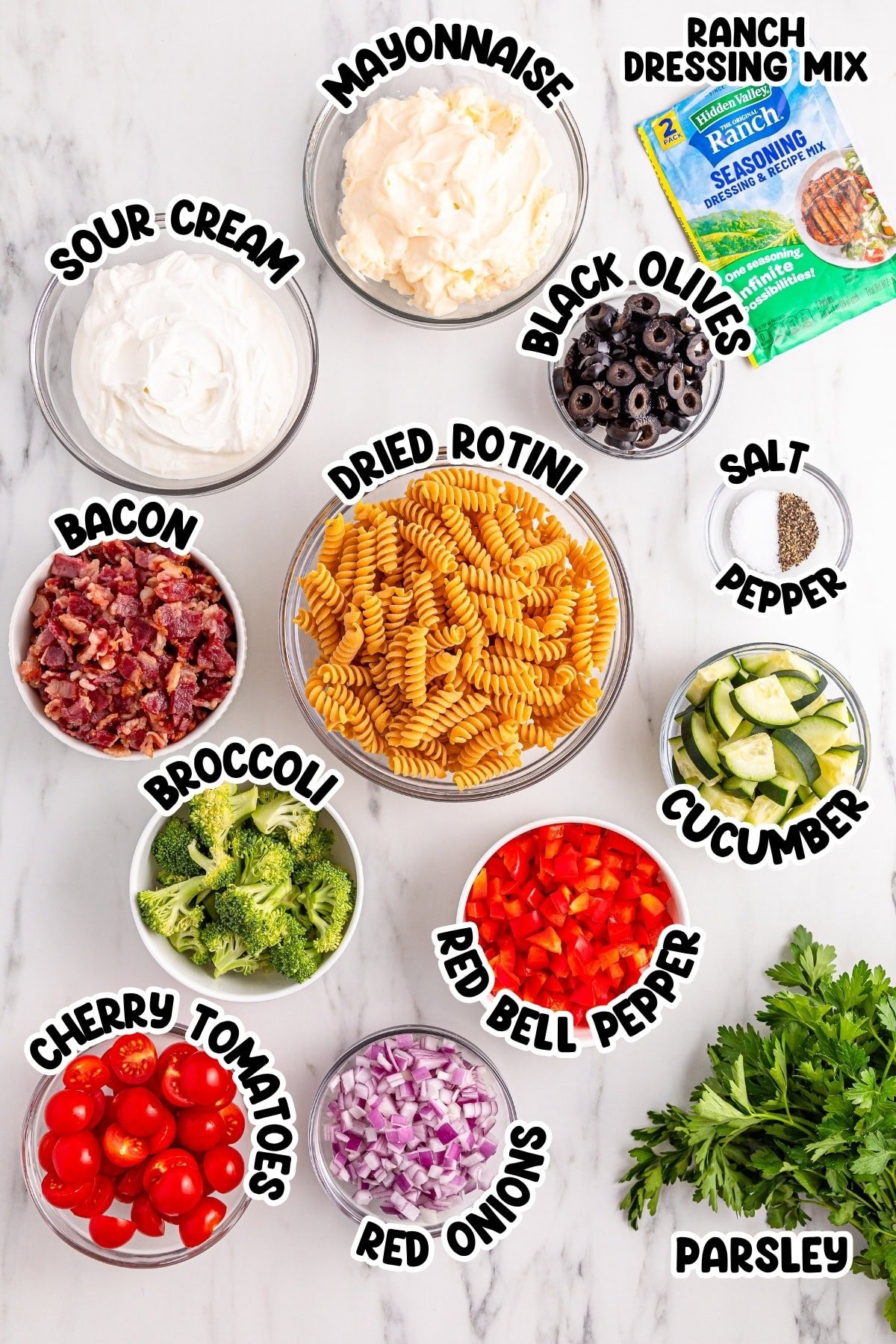 Ingredients for a pasta salad arranged in bowls, labeled with names of each item.