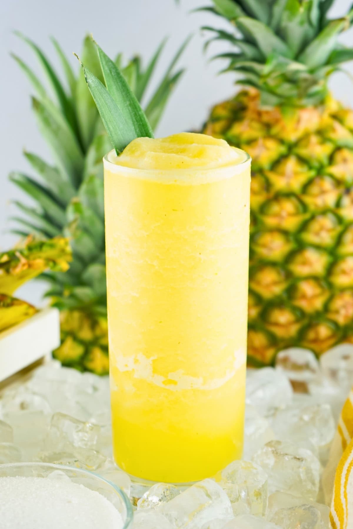 A yellow frozen pineapple drink in a glass, garnished with a pineapple leaf.