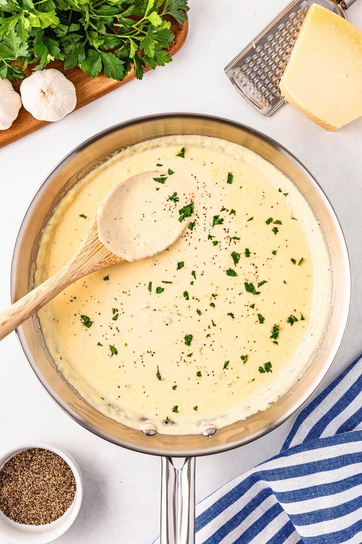 Creamy white sauce in a pan, garnished with herbs, with a wooden spoon.