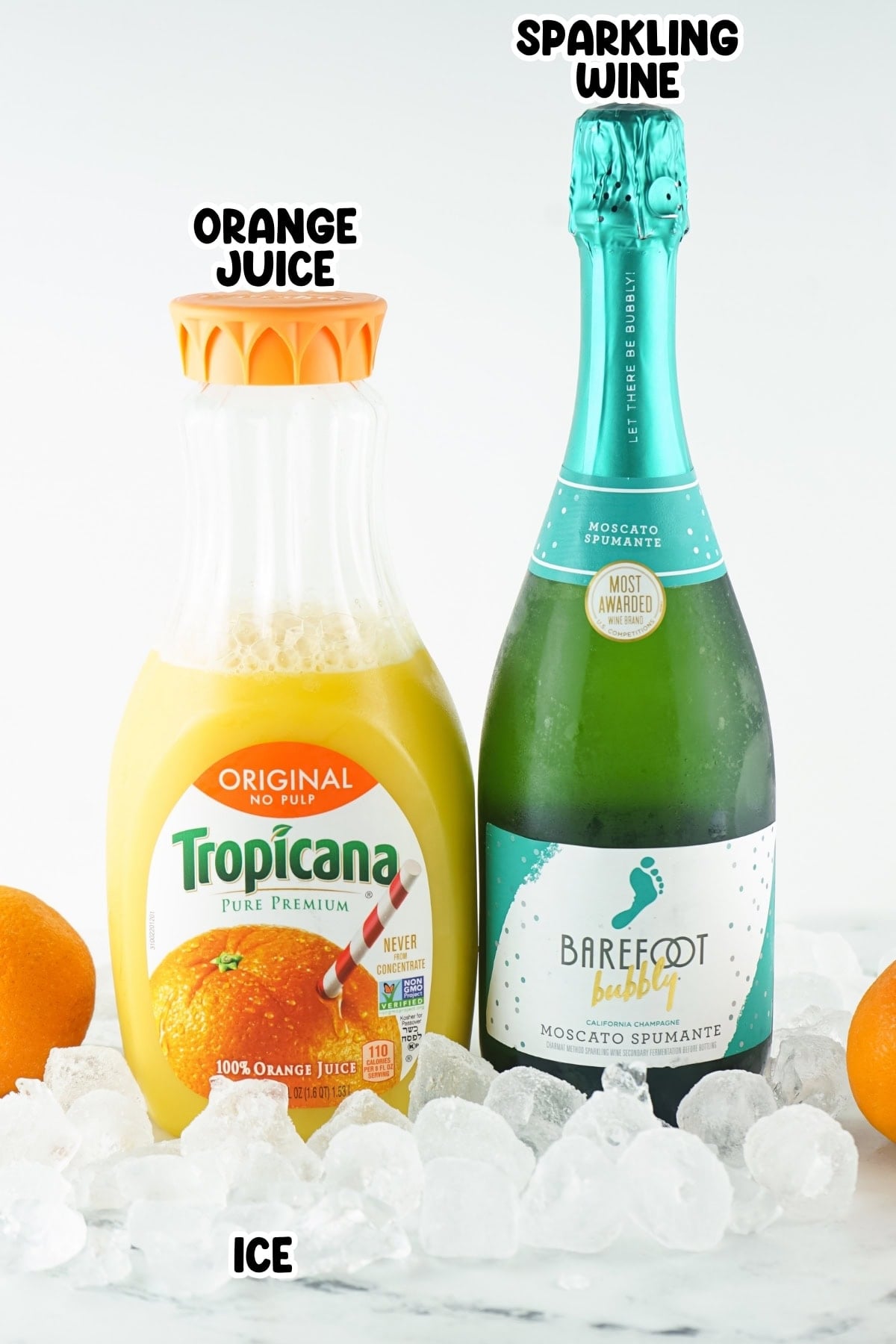 A bottle of orange juice and sparkling wine on ice with oranges nearby.