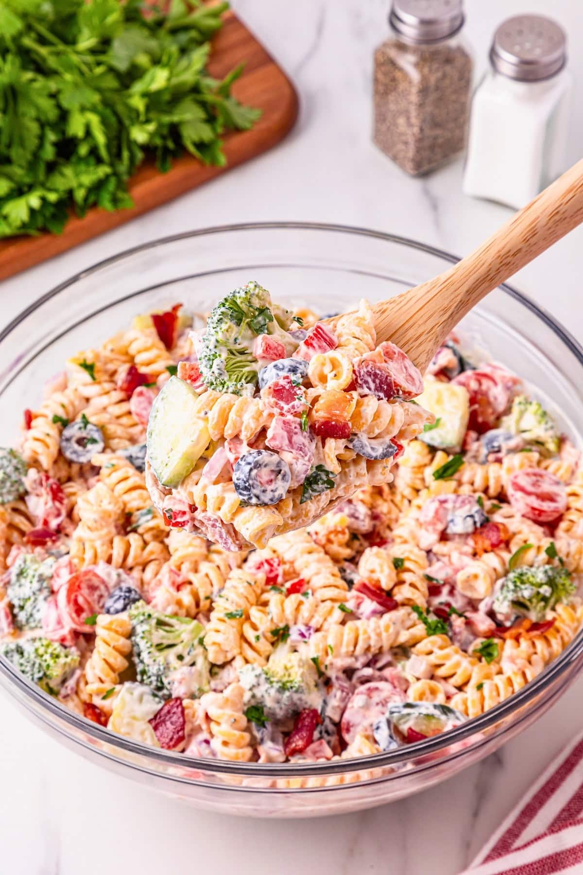 A bowl of creamy pasta salad with veggies, served with a wooden spoon.