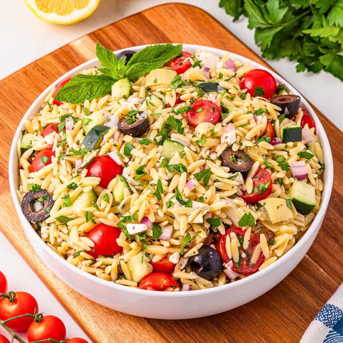 A bowl of orzo pasta salad recipe with tomatoes, olives, cucumber, and herbs.