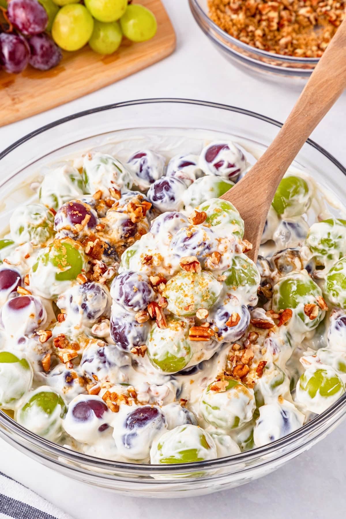 A bowl of creamy grape salad topped with chopped pecans and brown sugar.