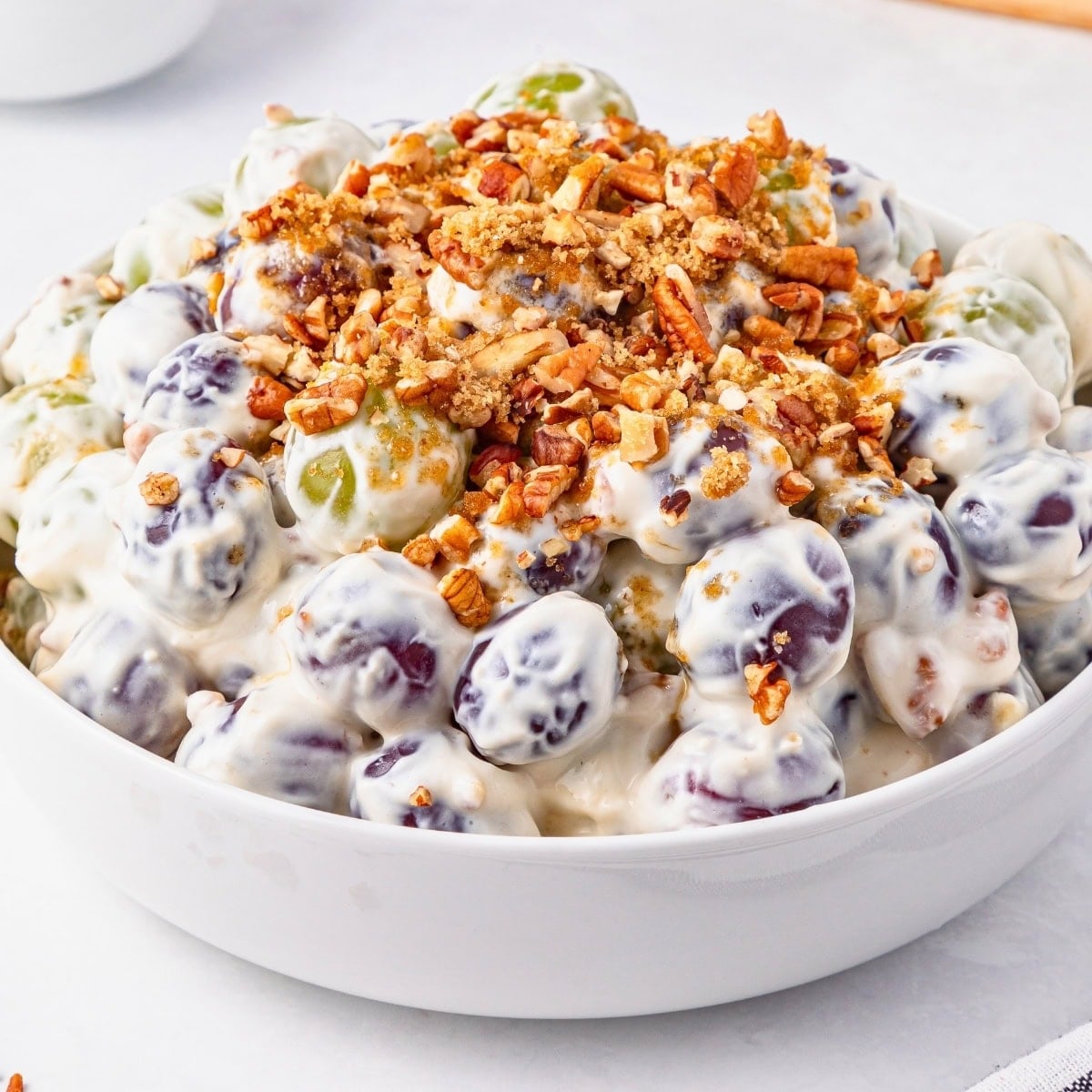 A bowl of creamy grape salad topped with chopped pecans.