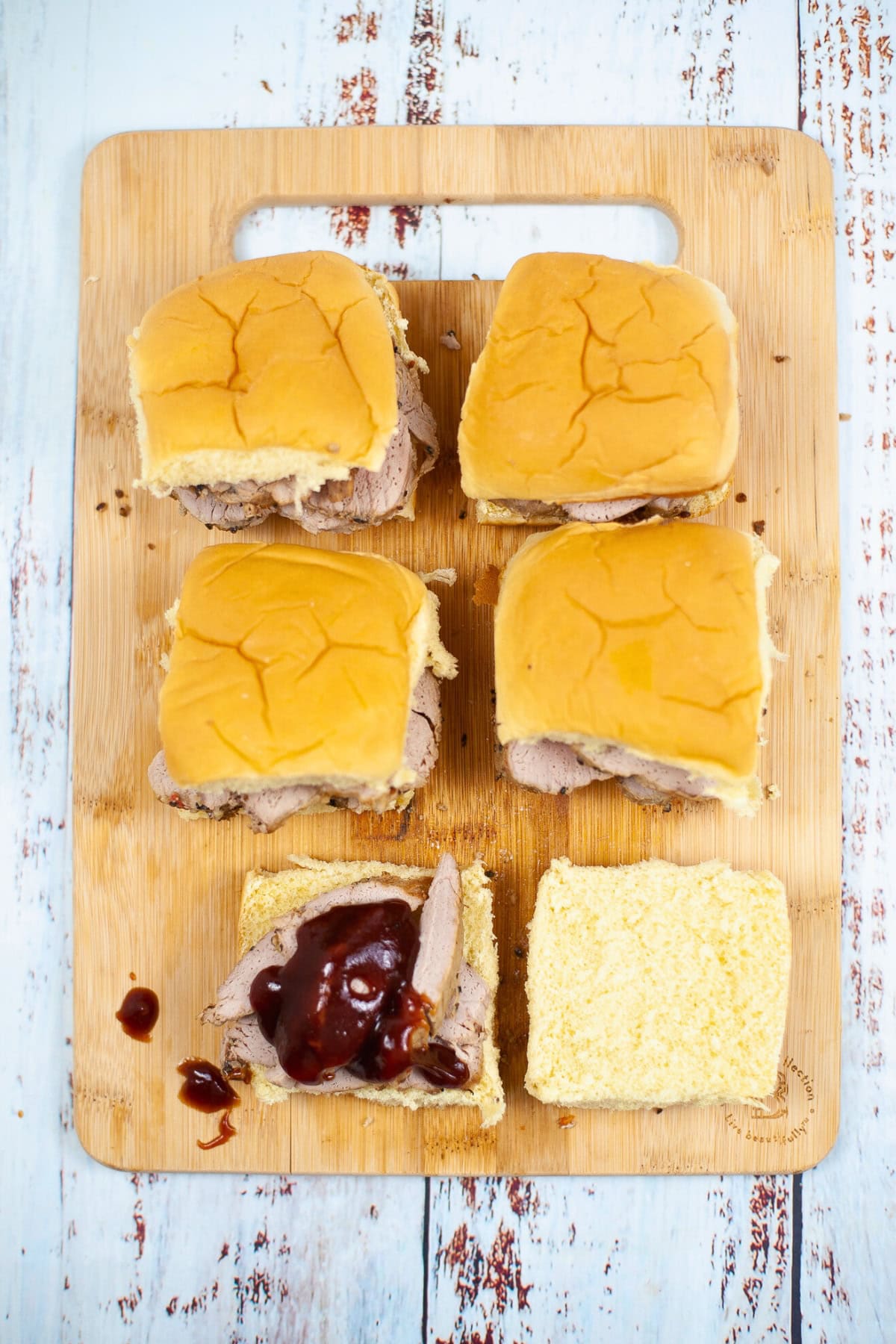 Four pulled pork sliders on a wooden board, one with barbecue sauce.