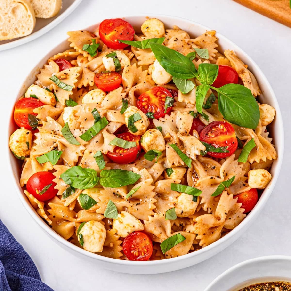 Bowl of farfalle pasta salad with cherry tomatoes, mozzarella, and fresh basil.