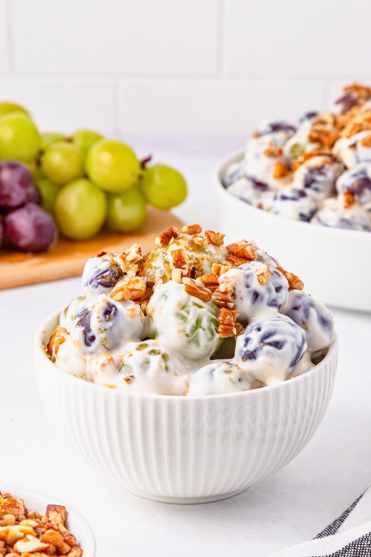 A white bowl of creamy grape salad topped with chopped pecans.
