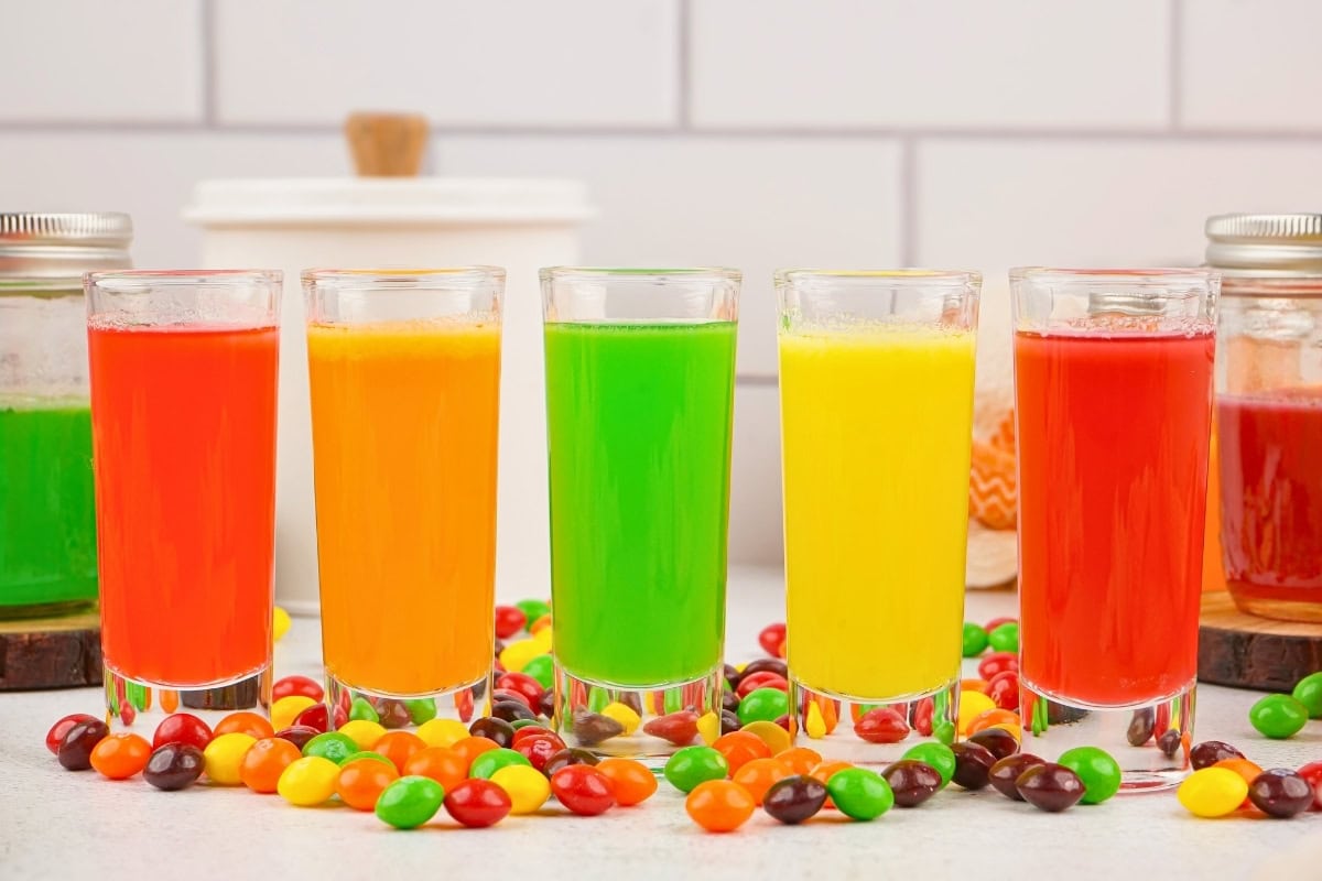 Five colorful vodka shots with Skittles candies scattered around them.