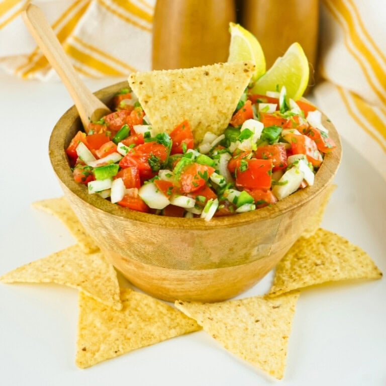 A wooden bowl of fresh salsa with tortilla chips and lime wedges.