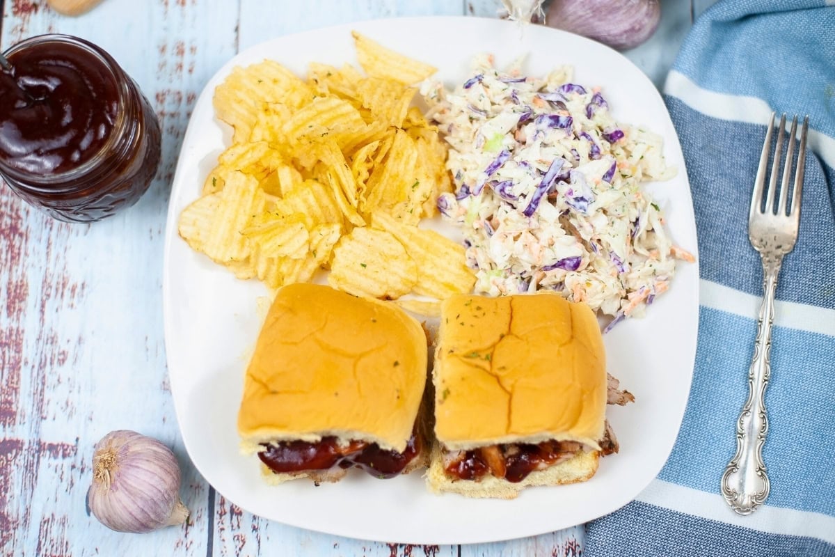 Plate with two sliders, potato chips, and coleslaw on a rustic wooden table.