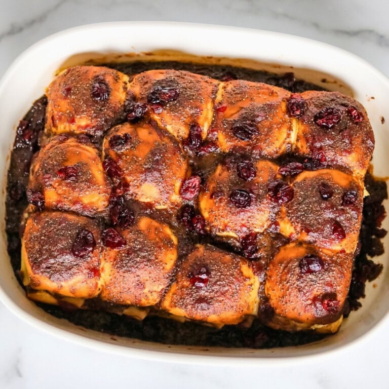 Baked sweet rolls topped with cinnamon and dried cranberries in a white dish.