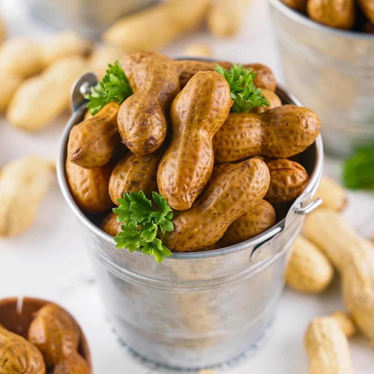 A small metal bucket filled with boiled peanuts and garnished with parsley.