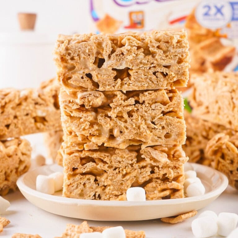Three golden cereal bars stacked on a plate with mini marshmallows around them.