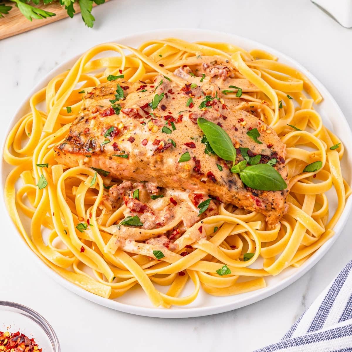 Creamy salmon fillet on fettuccine, garnished with basil and red pepper flakes.