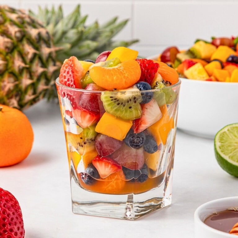 A glass filled with colorful mixed fruit salad, surrounded by fresh fruits.