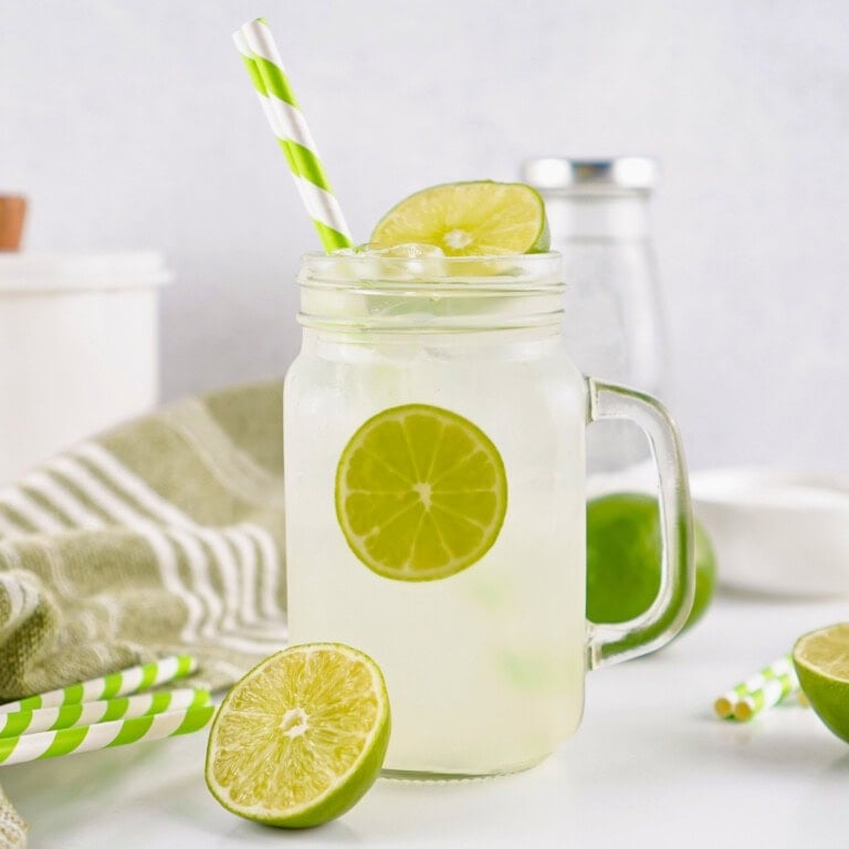 Iced lemonade in a mason jar with lime slices and green striped straws.