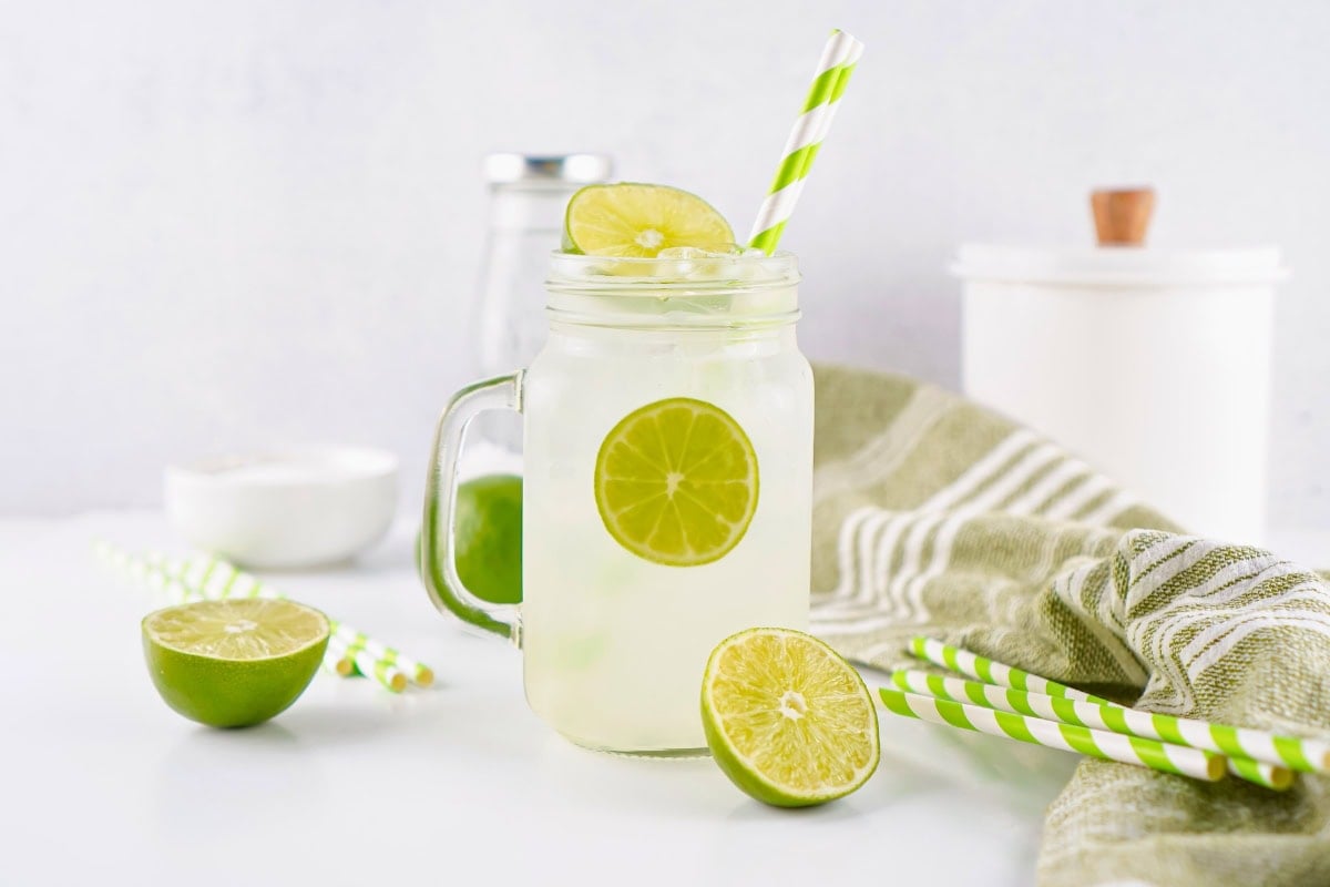 A glass of limeade with ice, lime slices, and green striped straws.