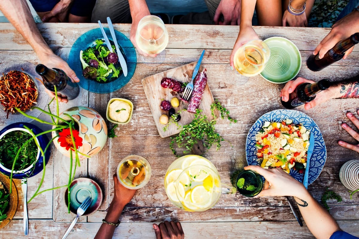 People sharing food and drinks around a rustic wooden table at a casual gathering.