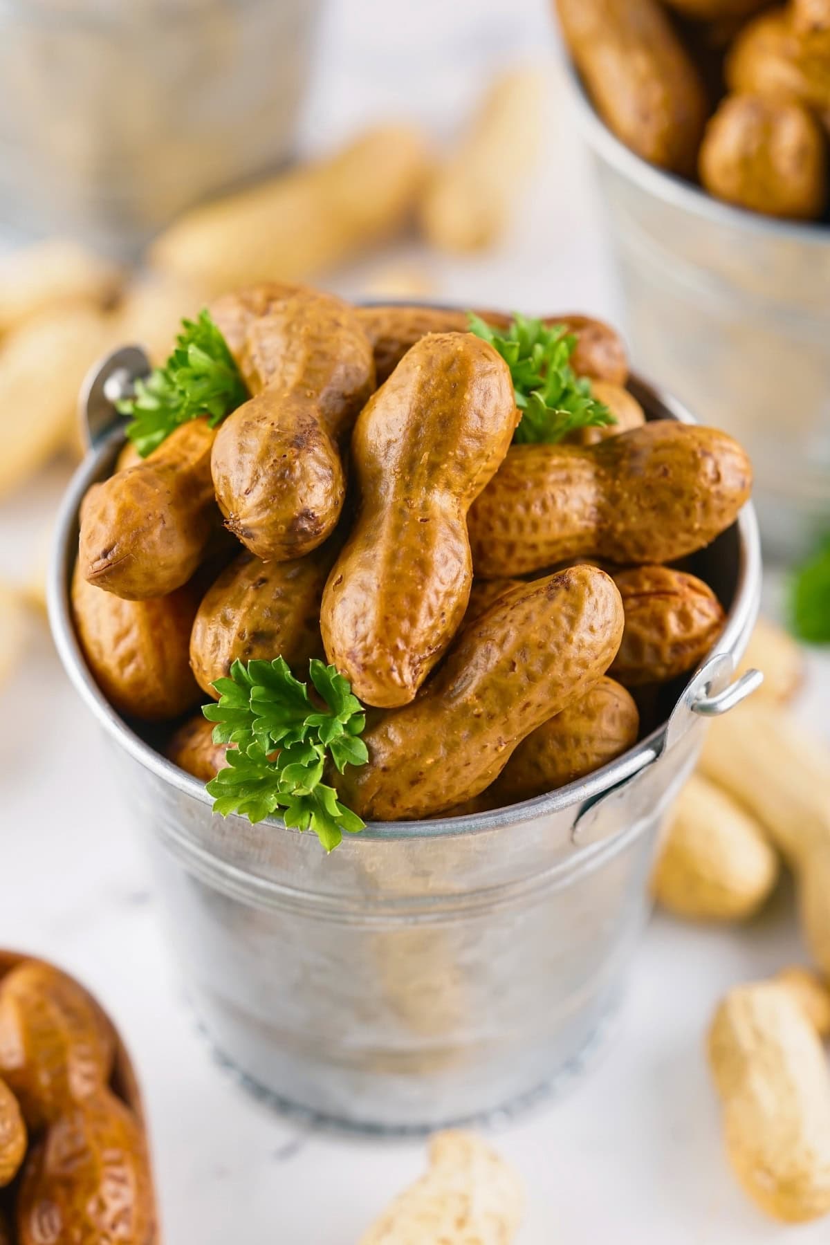 A small metal bucket filled with boiled peanuts and garnished with parsley.