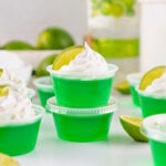 Green gelatin cups with whipped cream and lime wedges on top, surrounded by limes.