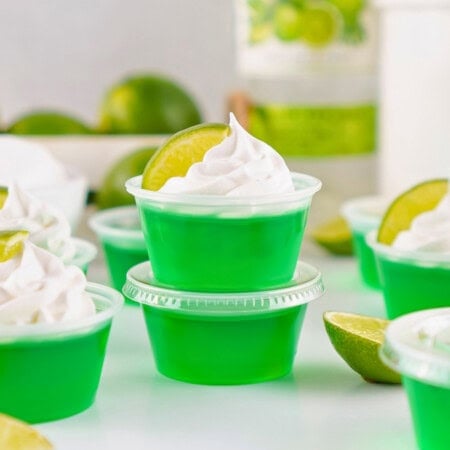 Green gelatin cups with whipped cream and lime wedges on top, surrounded by limes.
