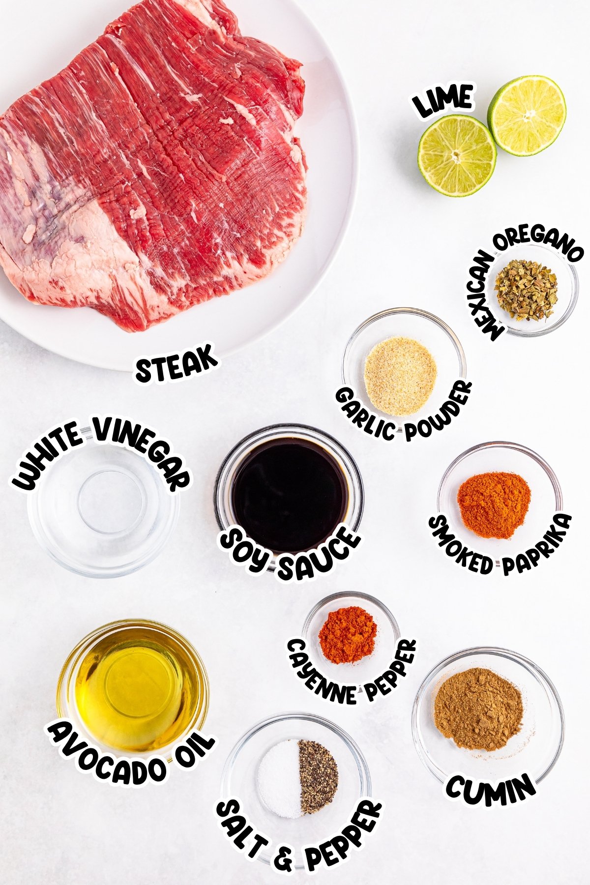 Raw steak, lime halves, various spices, oil, vinegar, and soy sauce on a white surface.