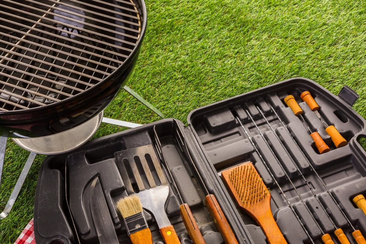 Outdoor grill and barbecue utensils set on grass, ready for grilling.