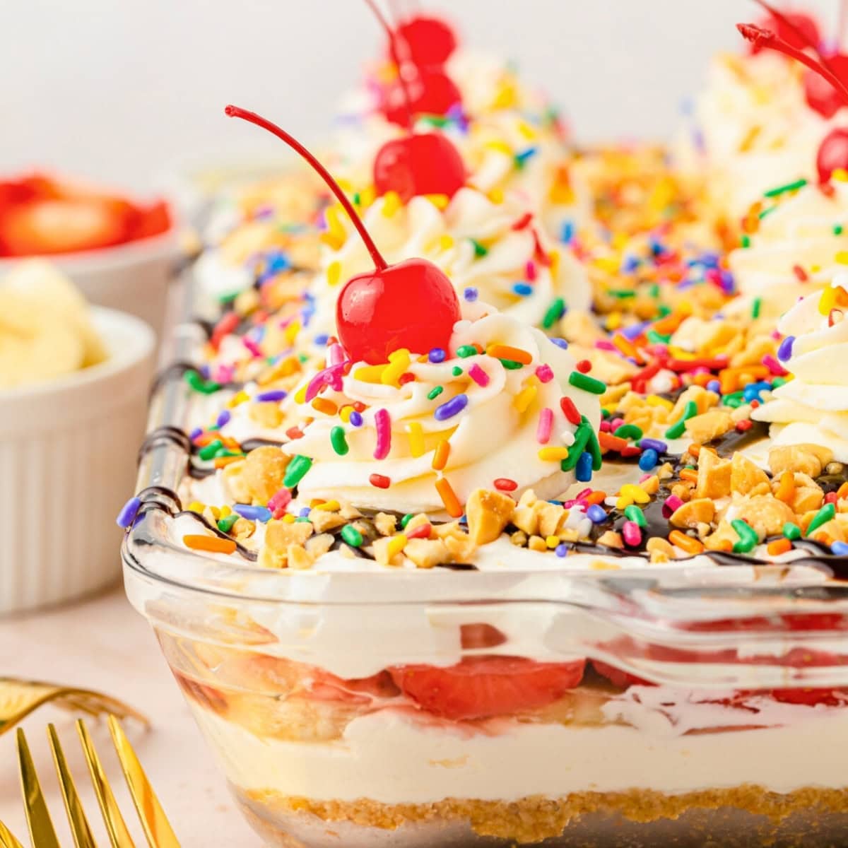 Glass dish of layered dessert with whipped cream, sprinkles, and cherries on top.