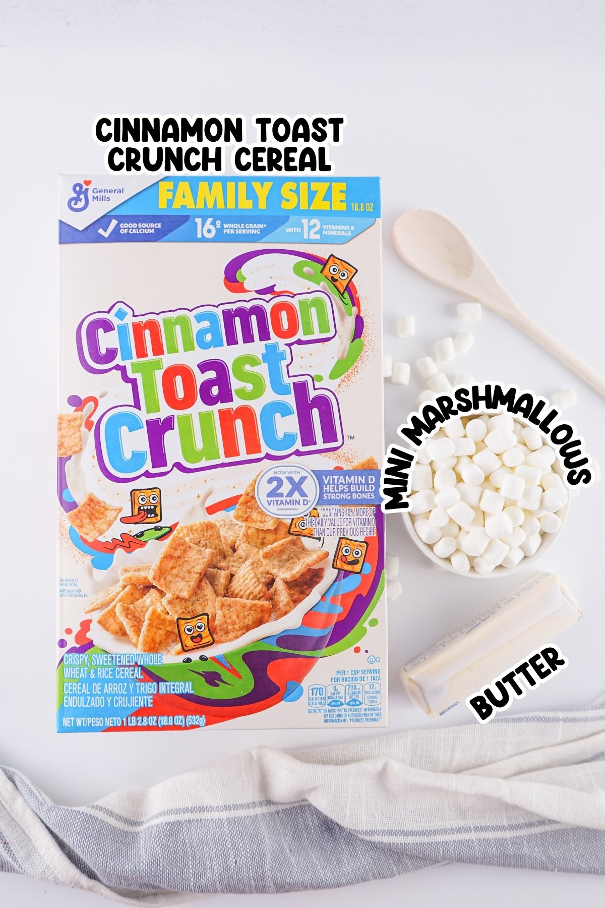 Box of Cinnamon Toast Crunch, mini marshmallows, butter, spoon, and towel on table.